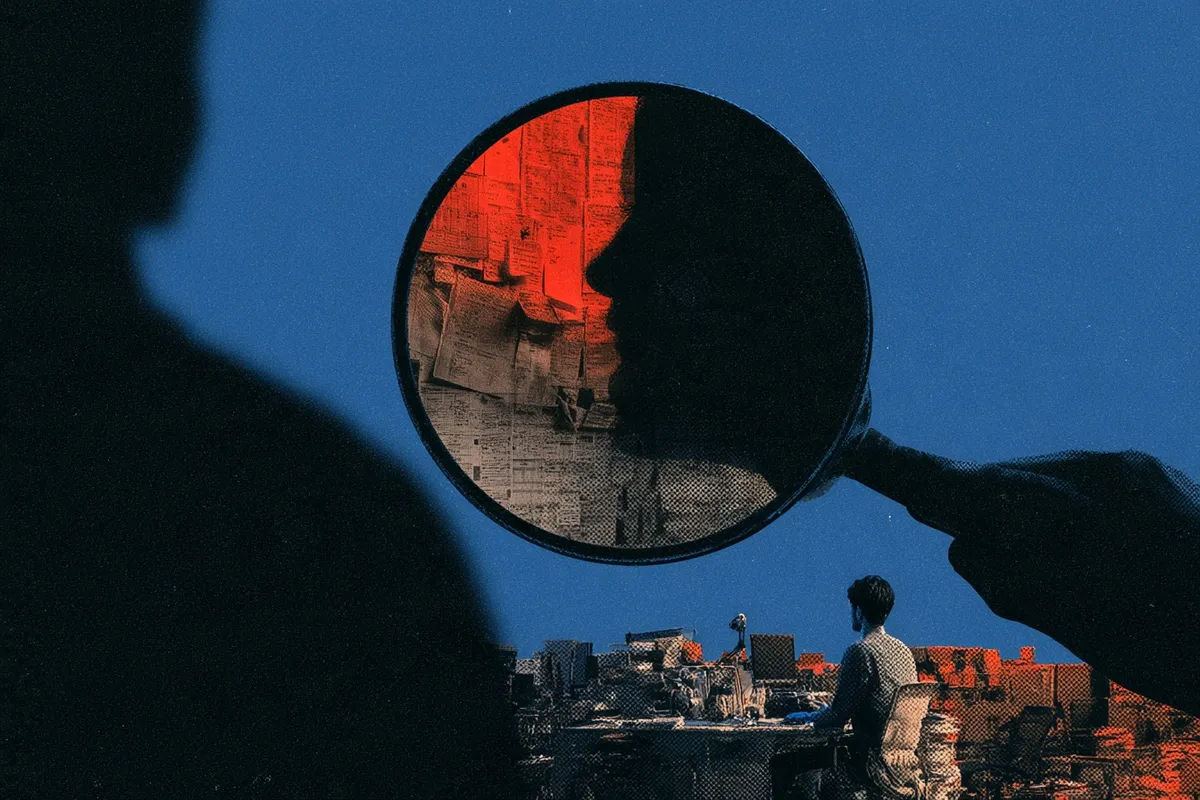 A silhouetted hand holds a magnifying glass over a wall of notes, above a worker at a cluttered desk